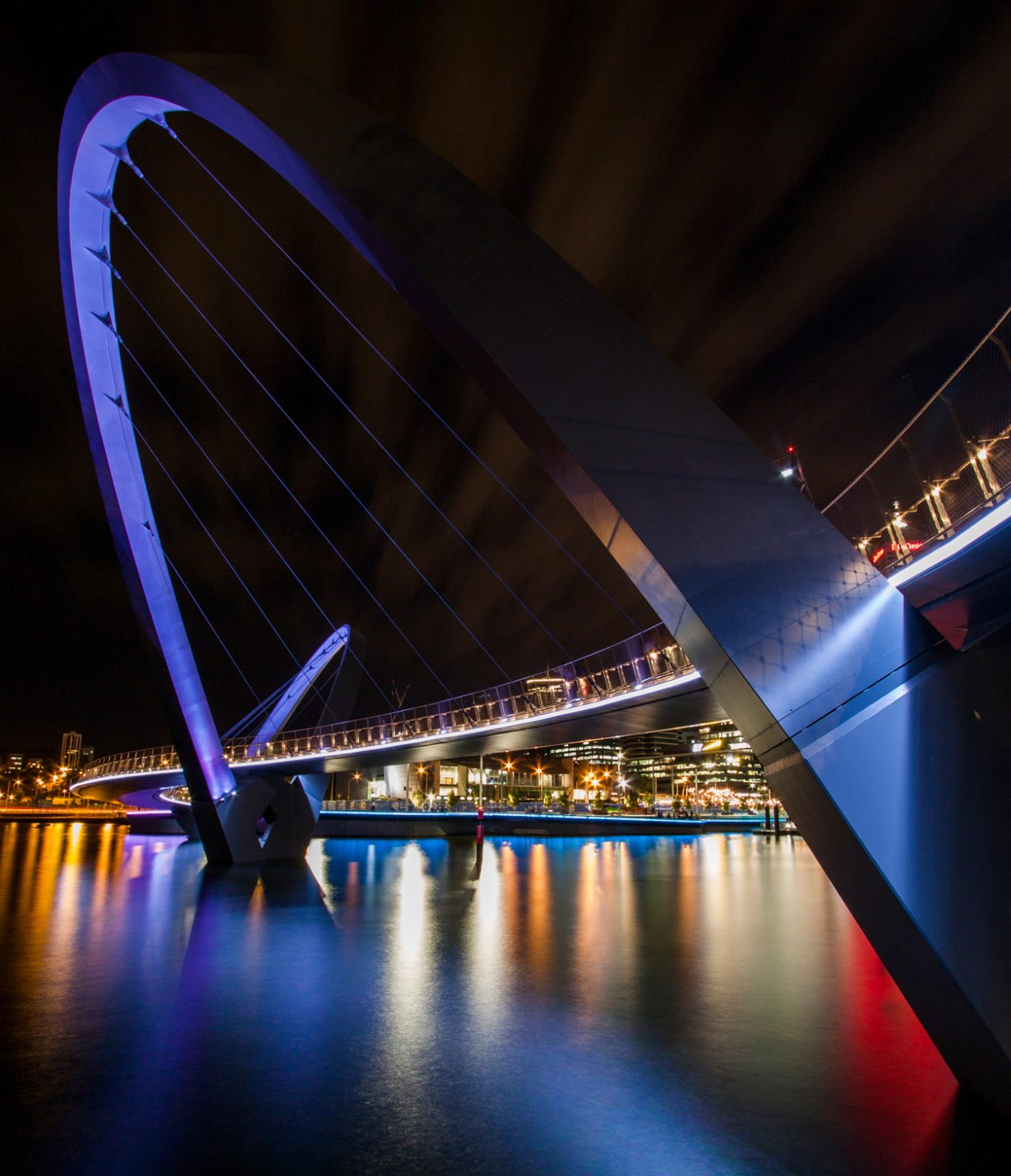 Angled view of Elizabeth Quay bridge's illuminated arch and cables.