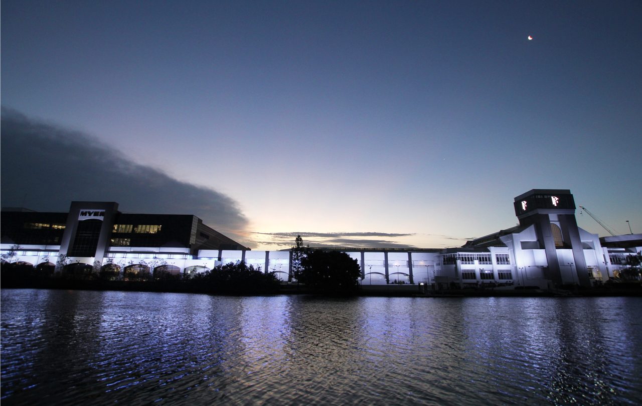 Panorama of Pacific Fair's illuminated riverfront beneath a fading evening sky.