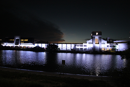 Wide view of Pacific Fair's white-lit facade across the river at night.