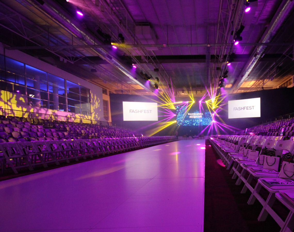Empty FashFest runway under purple and yellow lighting.