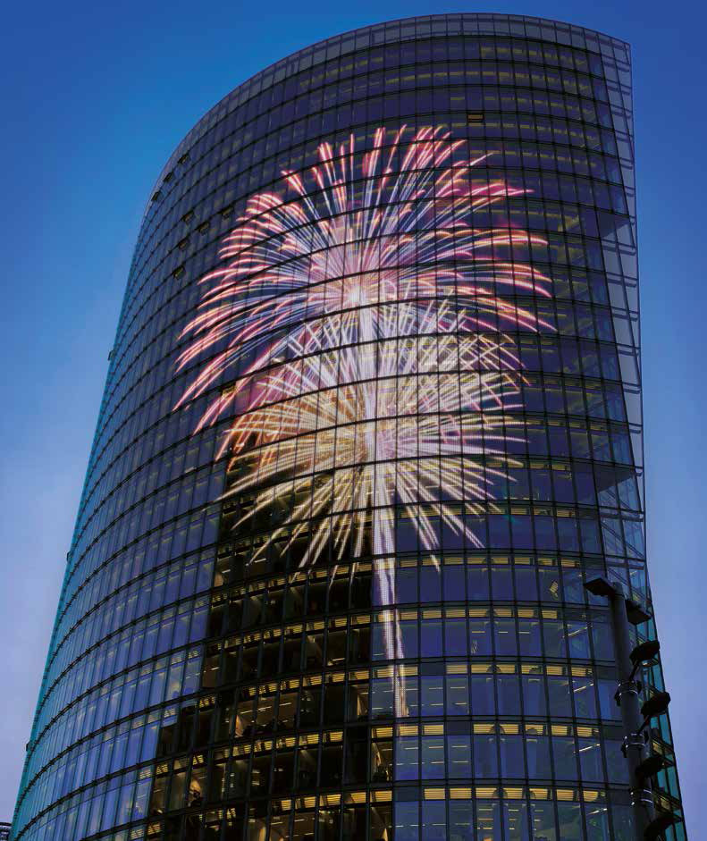 Colourful illuminated imagery across a curved glass tower facade at dusk.