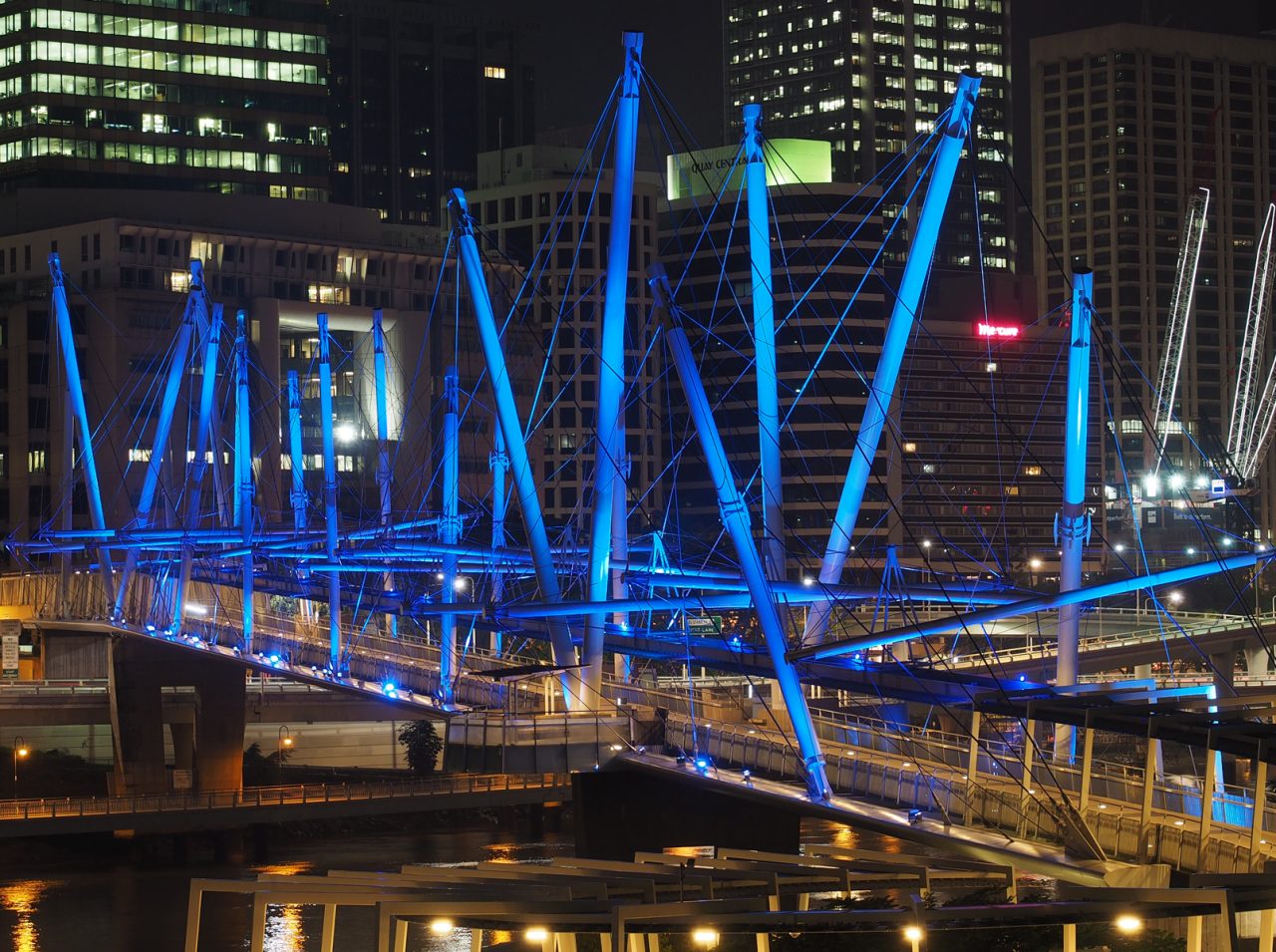 Blue-lit masts of Kurilpa Bridge against Brisbane's night skyline.