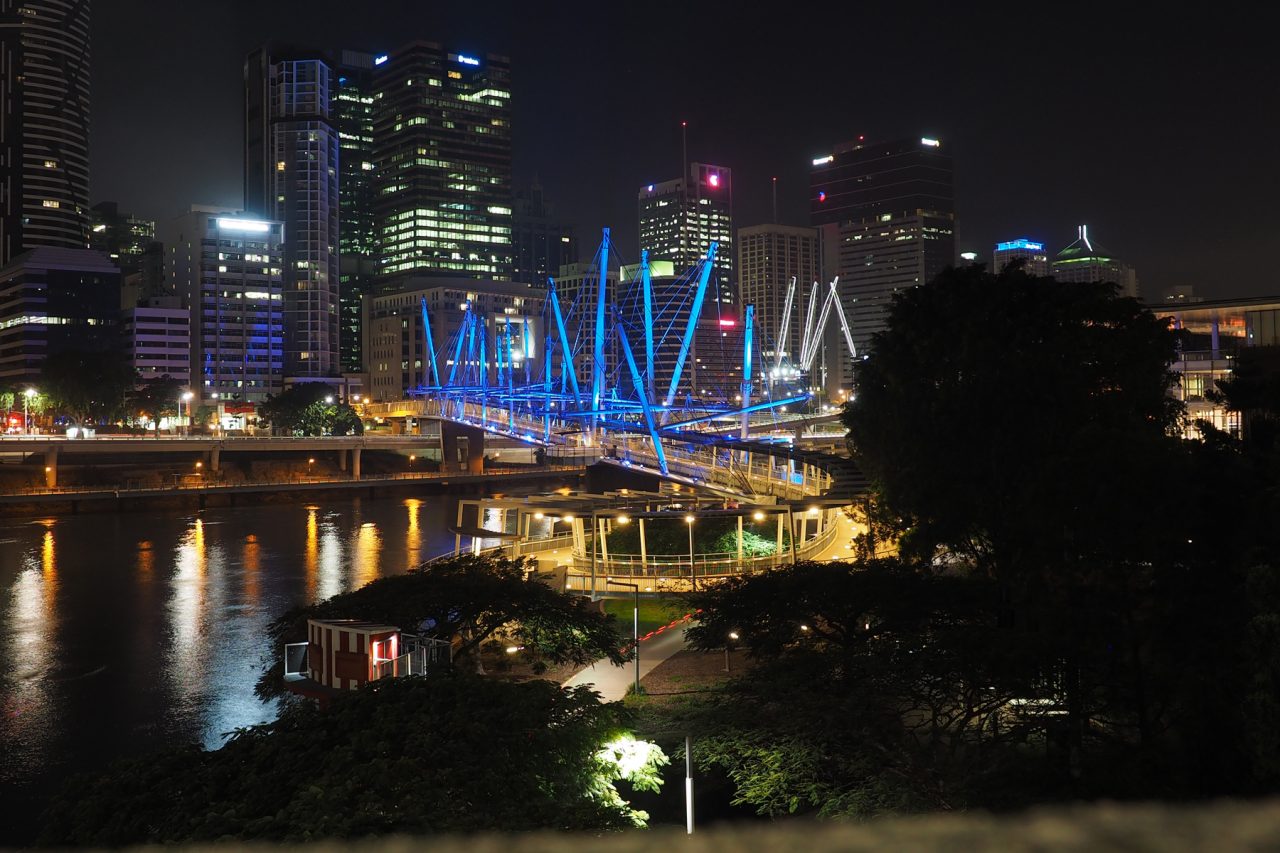 Wide view of blue-lit Kurilpa Bridge reflected in the river.