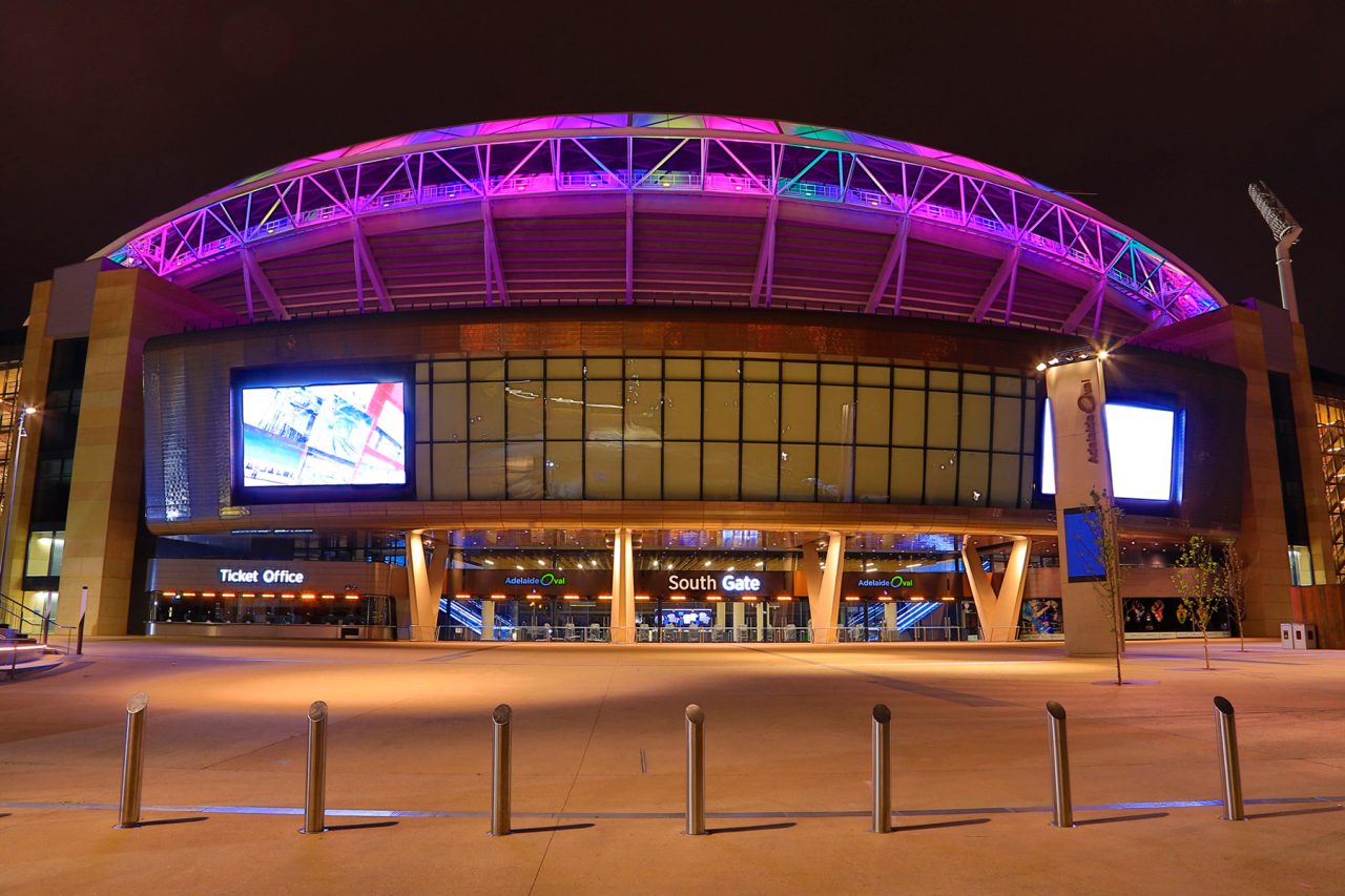 Adelaide Oval entrance beneath a roof lit purple at night.