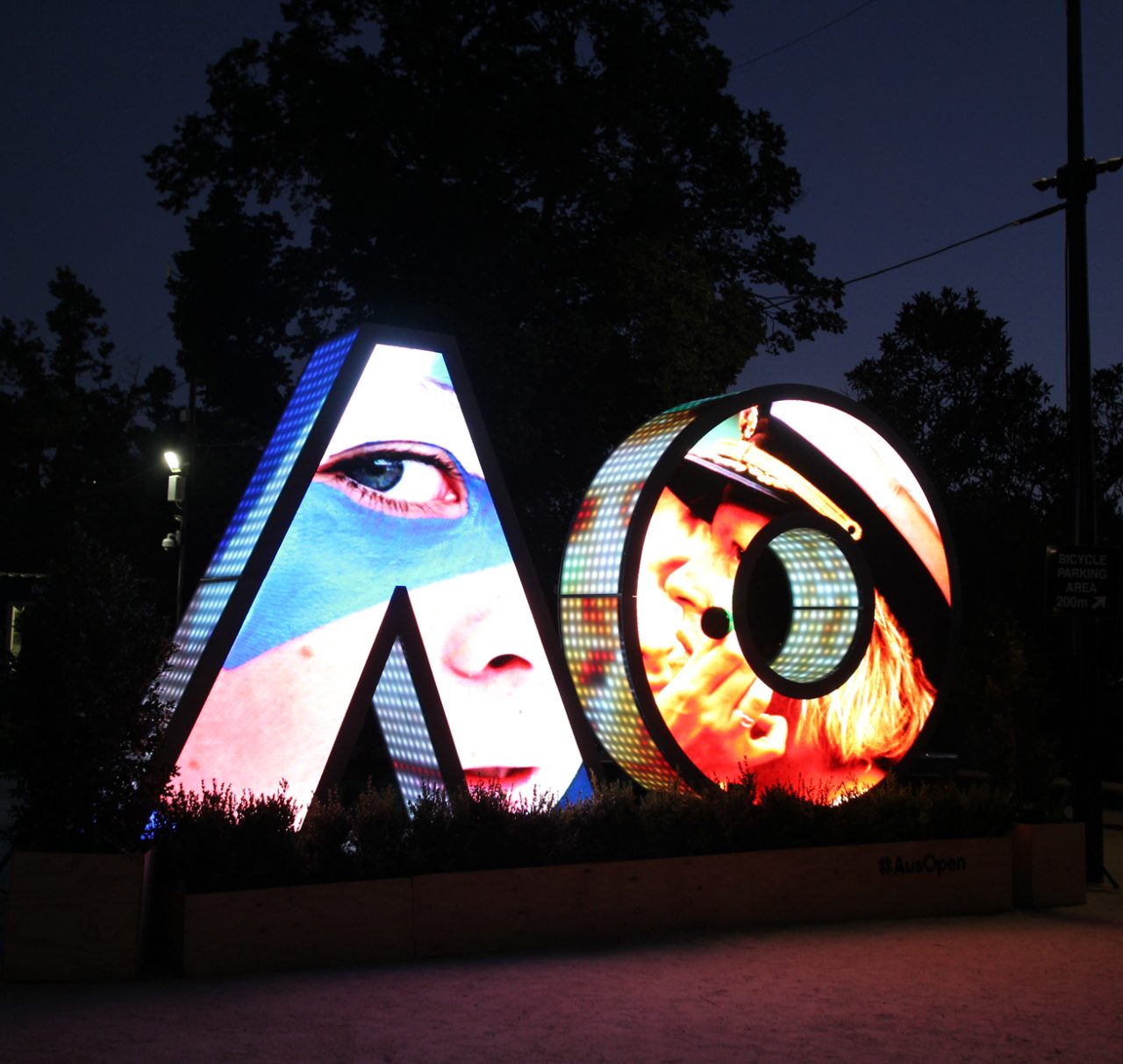 Portrait and graphic imagery across the illuminated AO sign at night.