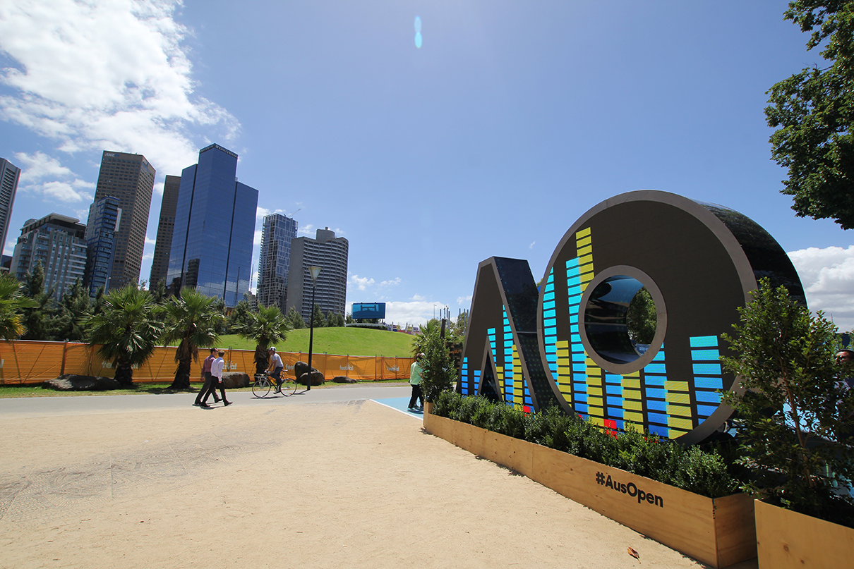 Side view of the AO digital sign with striped imagery and city buildings behind it.