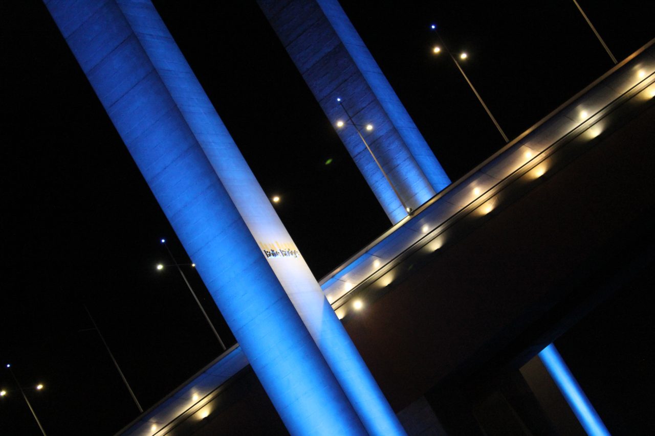 Close view beneath Bolte Bridge with its piers illuminated blue.