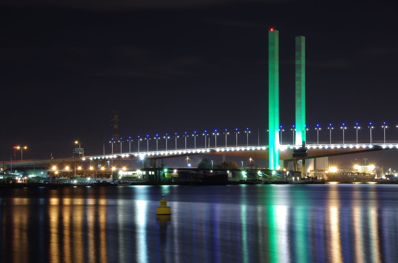 Green lighting on Bolte Bridge reflected in the water at night.