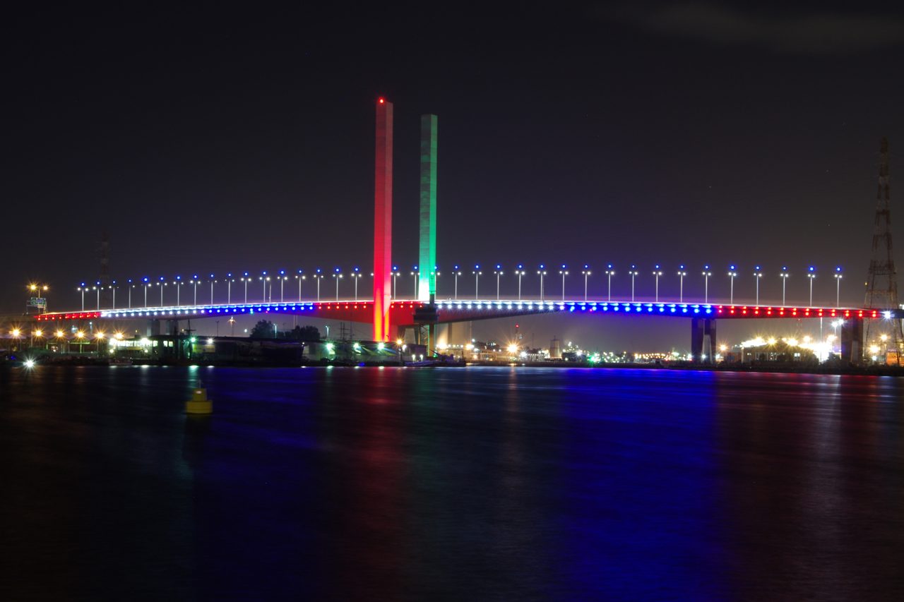 Bolte Bridge with red and green towers above a blue-lit deck, reflected in the water.