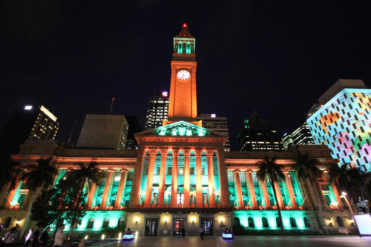 Brisbane City Hall illuminated in green and orange at night.