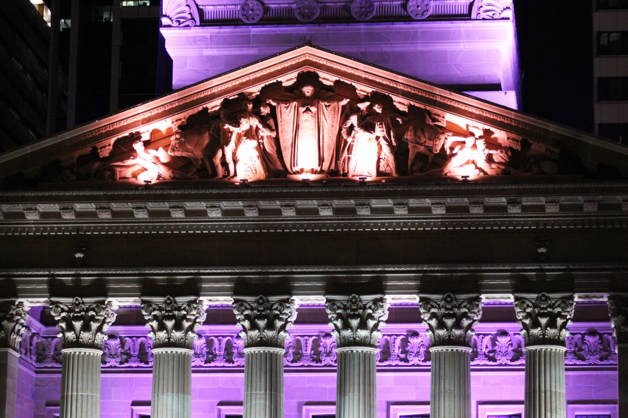Close view of Brisbane City Hall’s sculpted pediment and columns under coloured lighting.