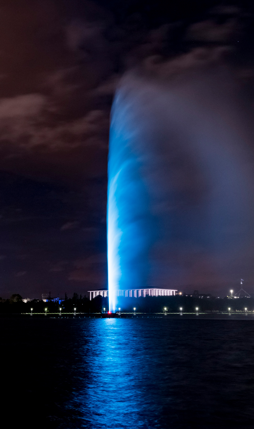 Captain Cook Memorial Jet illuminated blue above Lake Burley Griffin at night.