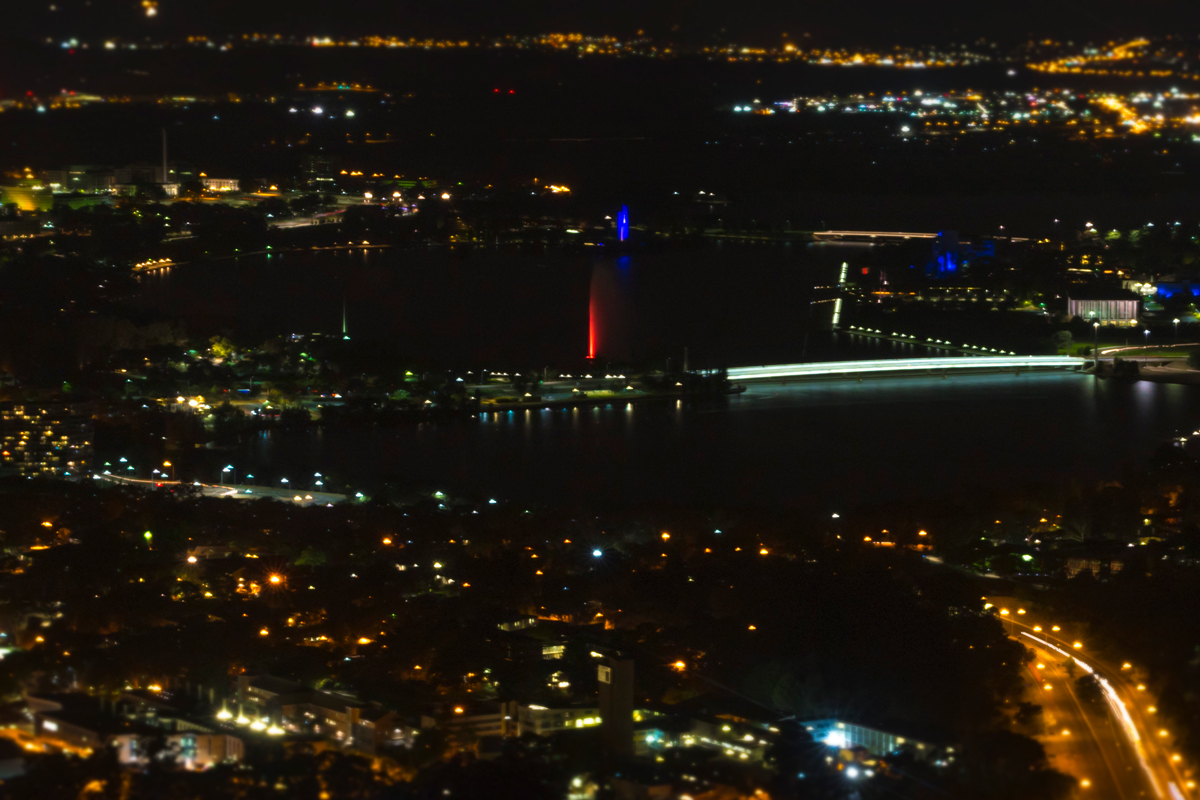 Aerial night view of Canberra and the illuminated memorial jet in Lake Burley Griffin.