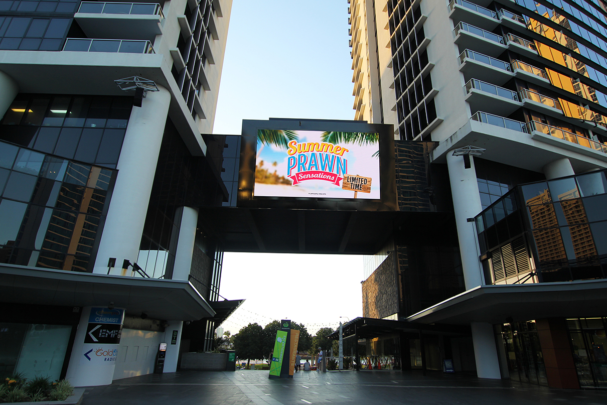 The outdoor screen at Circle on Cavill between sunlit towers in the evening.