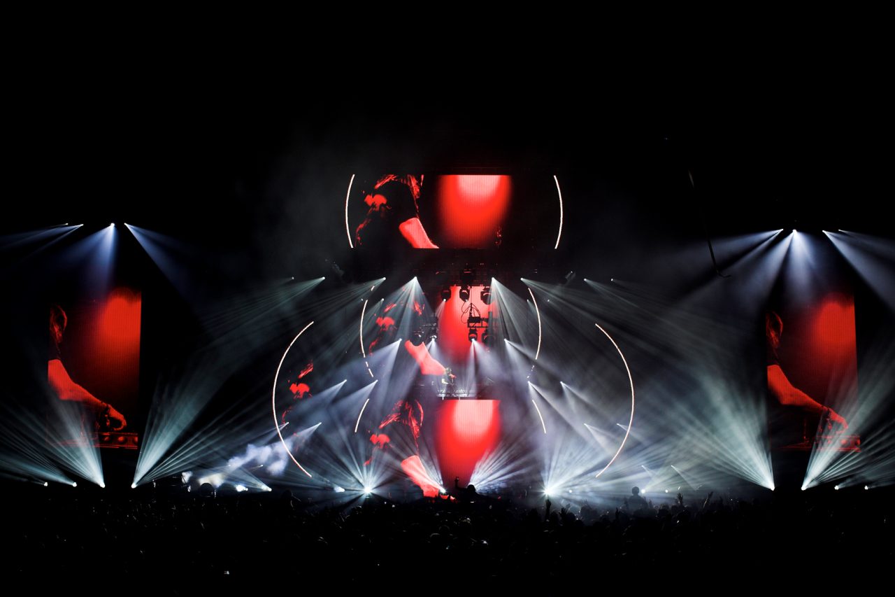 Red imagery on vertical video screens between white lighting beams at David Guetta's show.
