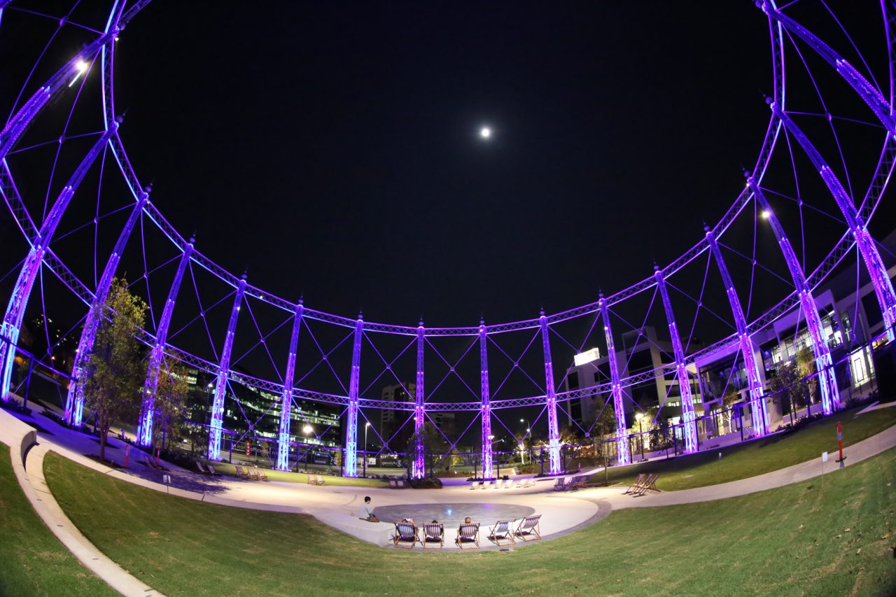 Wide view looking up through the purple-lit gasometer framework at Gasworks Plaza.