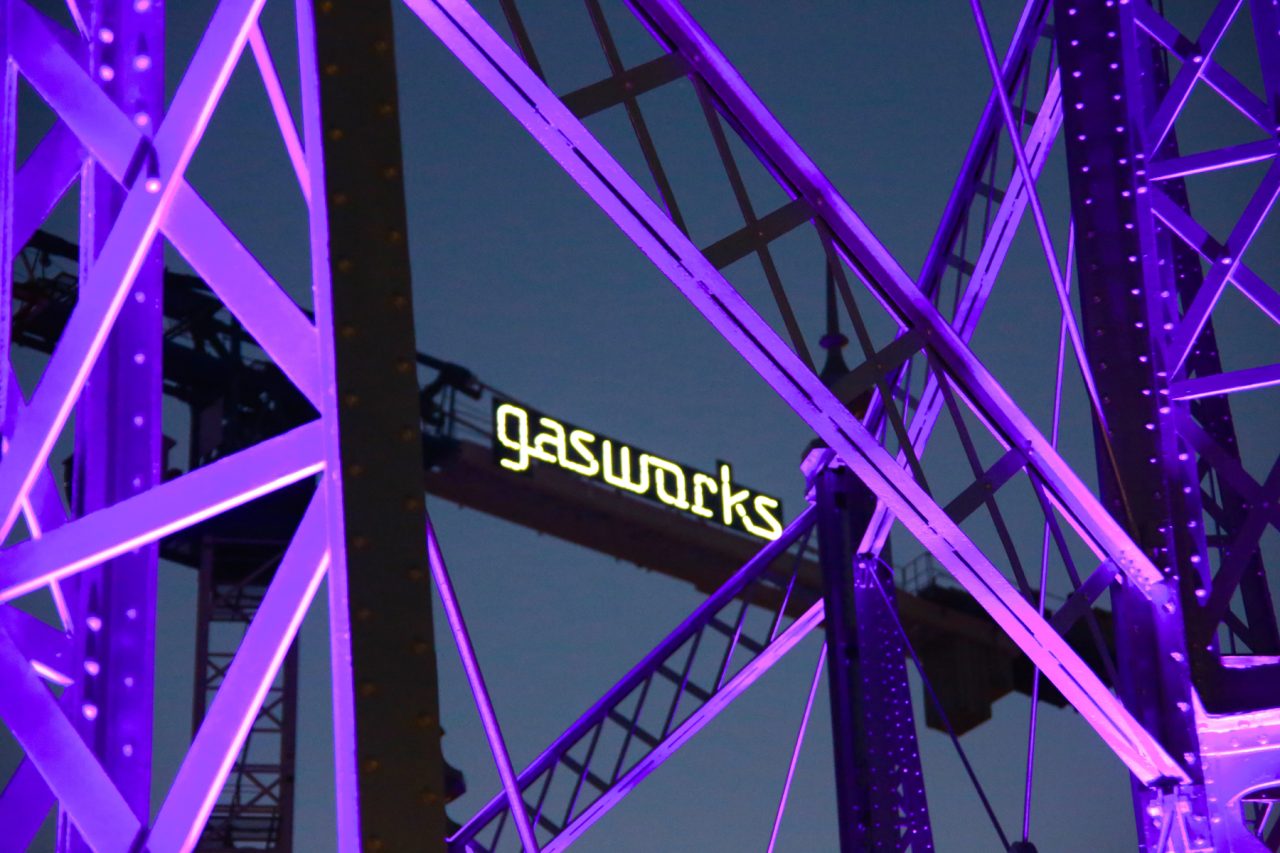 Purple lighting on the gasometer framework and Gasworks Plaza sign.