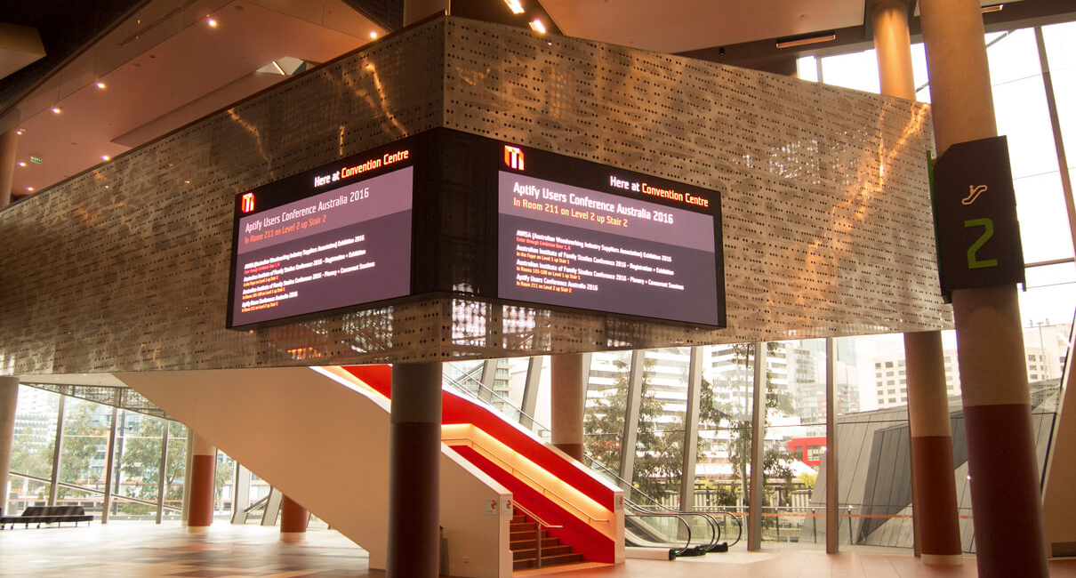 Wide view of the paired event information screens beside an escalator at MCEC.