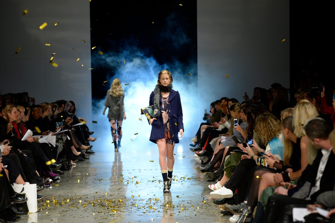 Models walk along a reflective runway between seated guests at New Zealand Fashion Week.