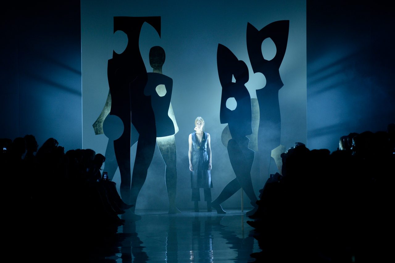 Models emerge through a sculptural backdrop with blue lighting at New Zealand Fashion Week.