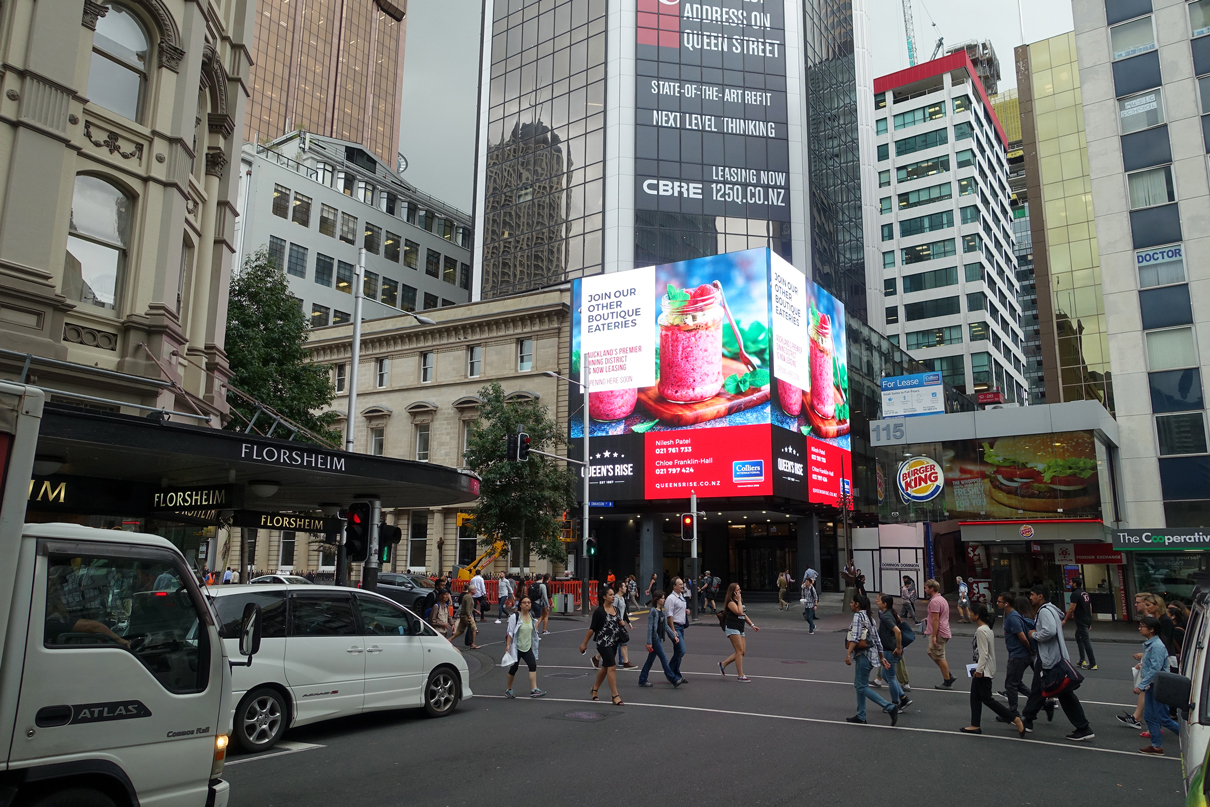Colourful advertising on the wraparound Queen's Rise media facade above the busy street corner.