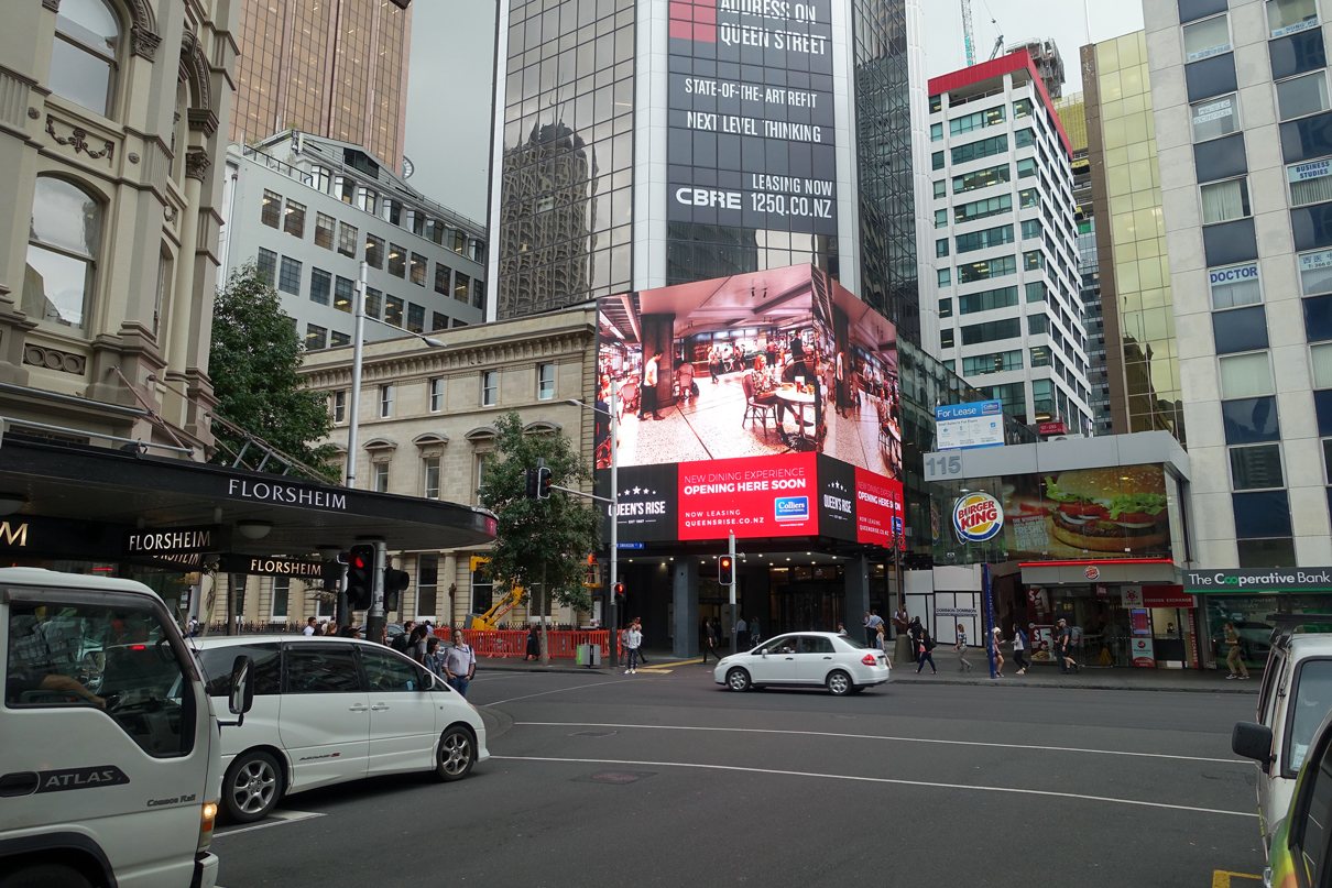 Traffic passes the Queen's Rise building beneath its wraparound advertising screen.