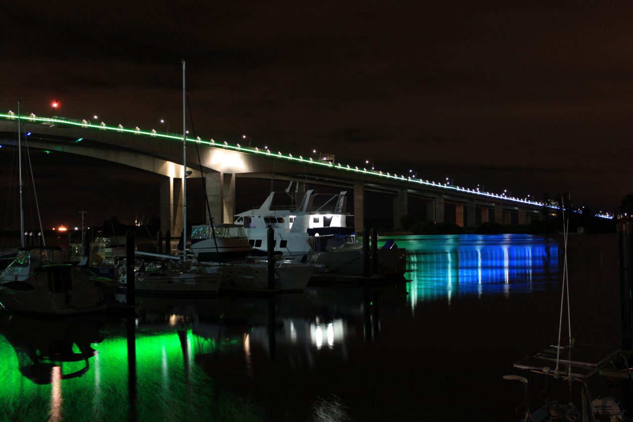 Blue and green lighting along Sir Leo Hielscher Bridges reflected in the river.