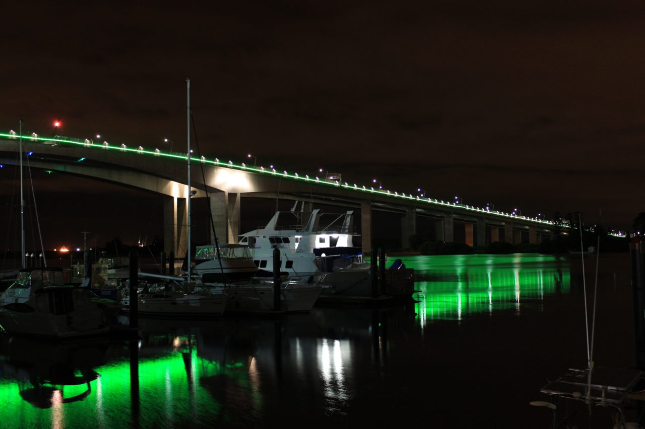 Green architectural lighting reflected in the river beneath Sir Leo Hielscher Bridges.