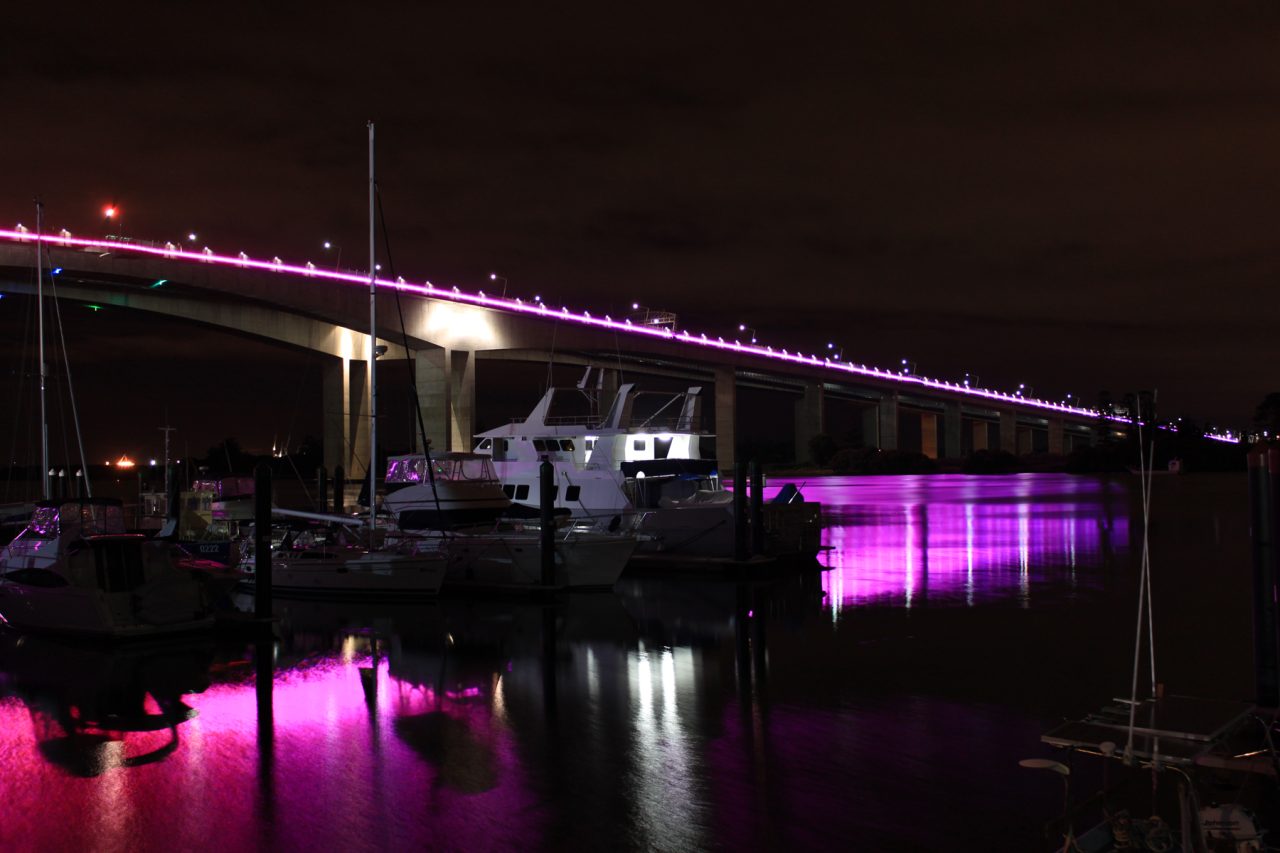 Purple and pink lighting reflected beneath Sir Leo Hielscher Bridges at night.