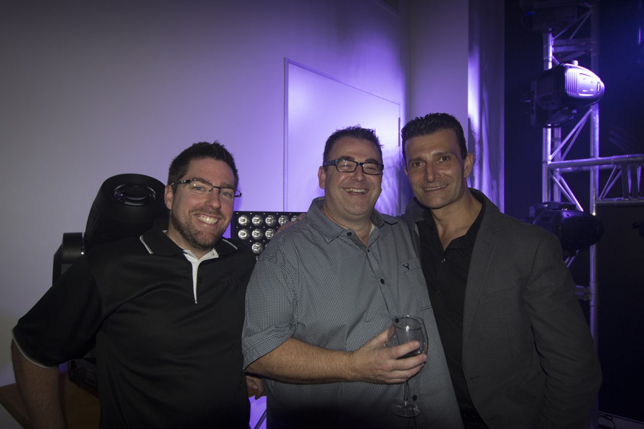 Three guests posing beside a purple-lit lighting display.
