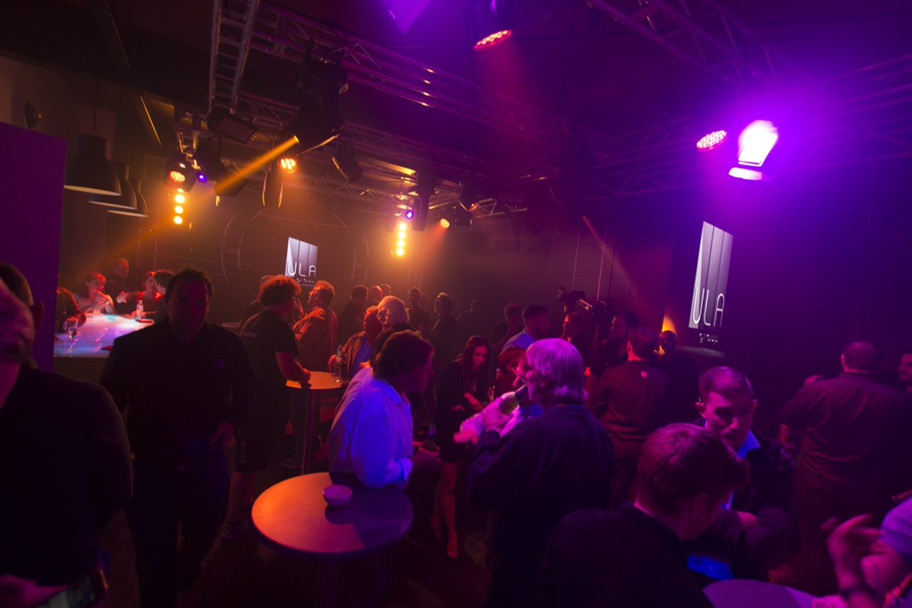 Guests gathered around tables under purple showroom lighting.