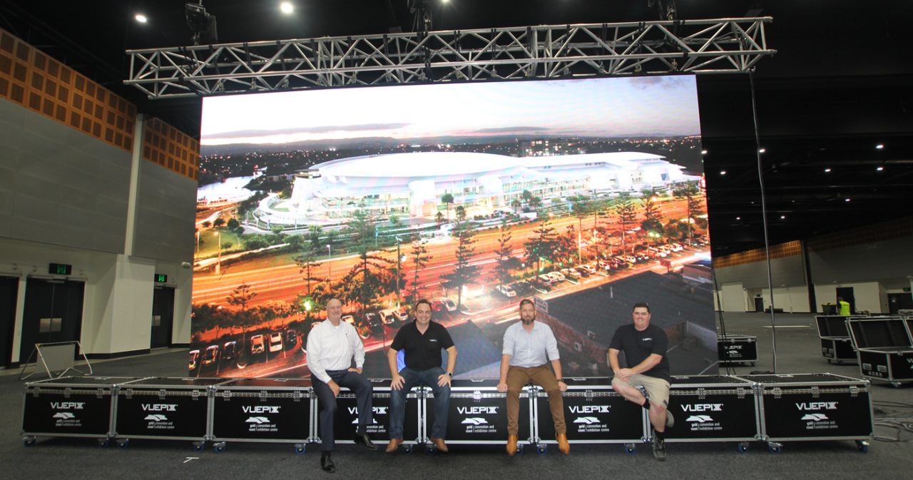Team members standing beside flight cases beneath a large landscape display.