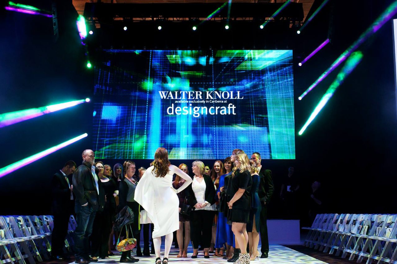 A group on the FashFest runway beneath designer branding on the central screen.