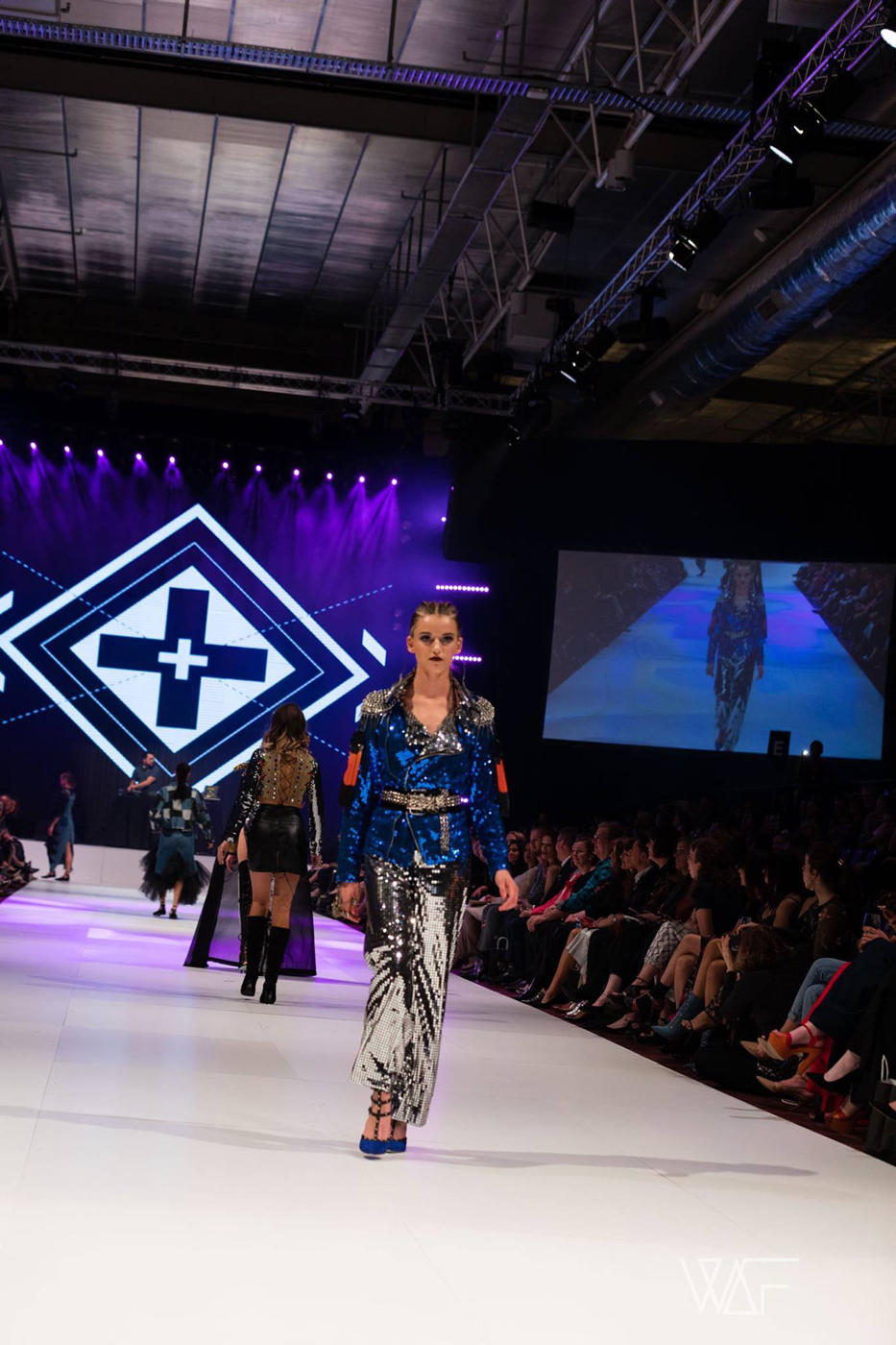 Model in a patterned outfit on the FashFest runway in front of geometric LED graphics.