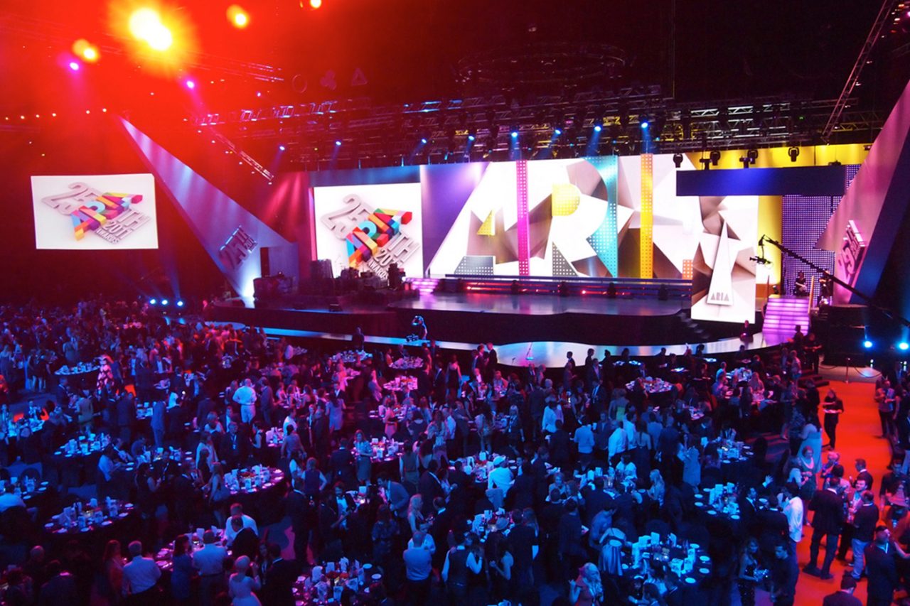 Red lighting over the ARIA Awards audience facing the large video backdrop.