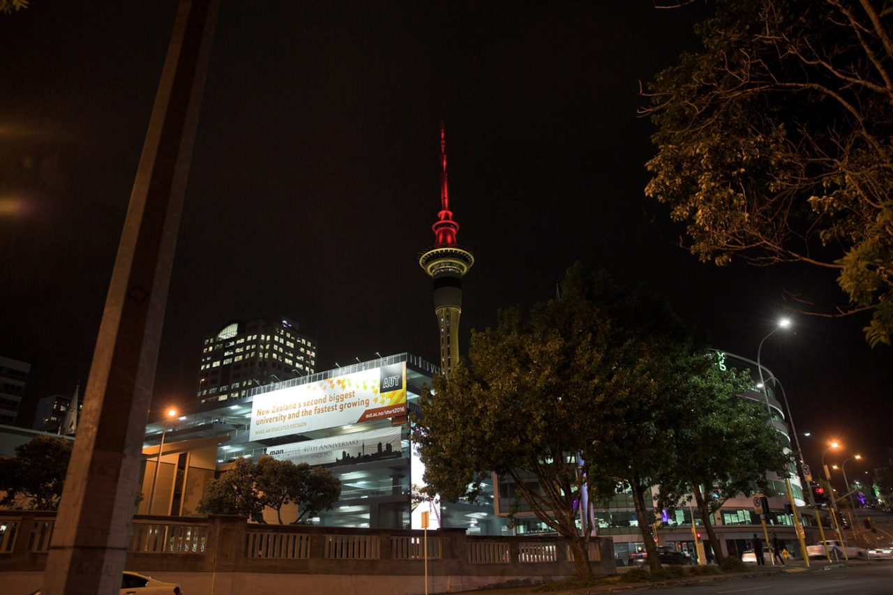 Sky Tower's illuminated upper spire above Auckland streets at night.