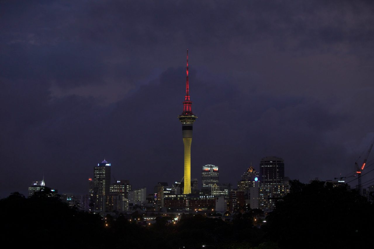 Auckland's Sky Tower illuminated yellow with a red upper spire above the night skyline.