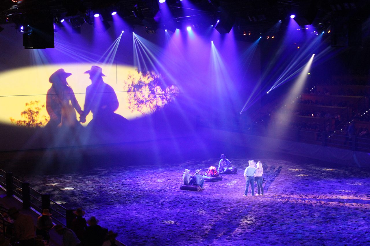 Riders in a purple-lit arena beneath a large screen at Australian Outback Spectacular.