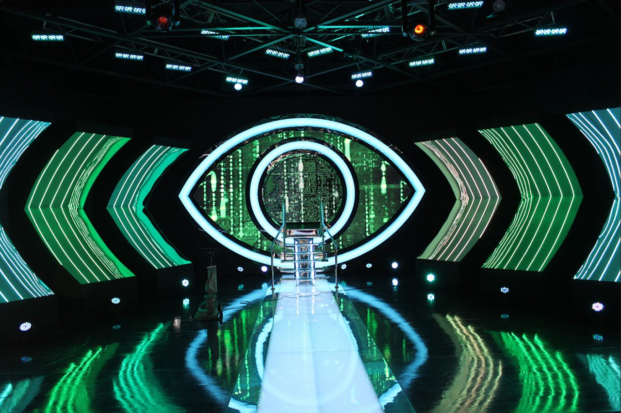 Green eye graphics on the Big Brother stage screens above the reflective runway.