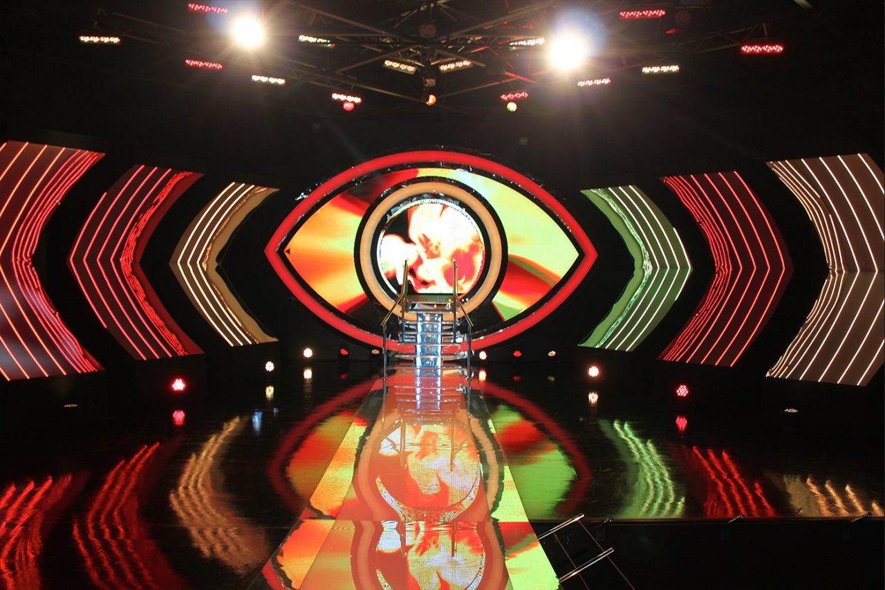 Orange and red eye graphics across the Big Brother stage screens.