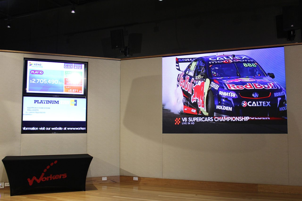 Racing-car imagery on the large screen beside smaller information displays at Blacktown Workers Club.