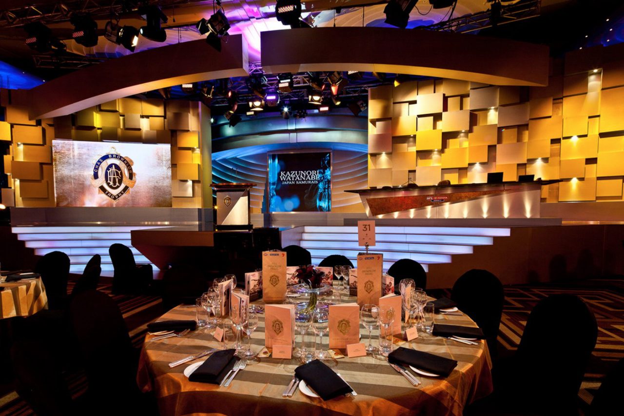 Banquet tables facing the gold stage and digital screens at the Brownlow Medal event.
