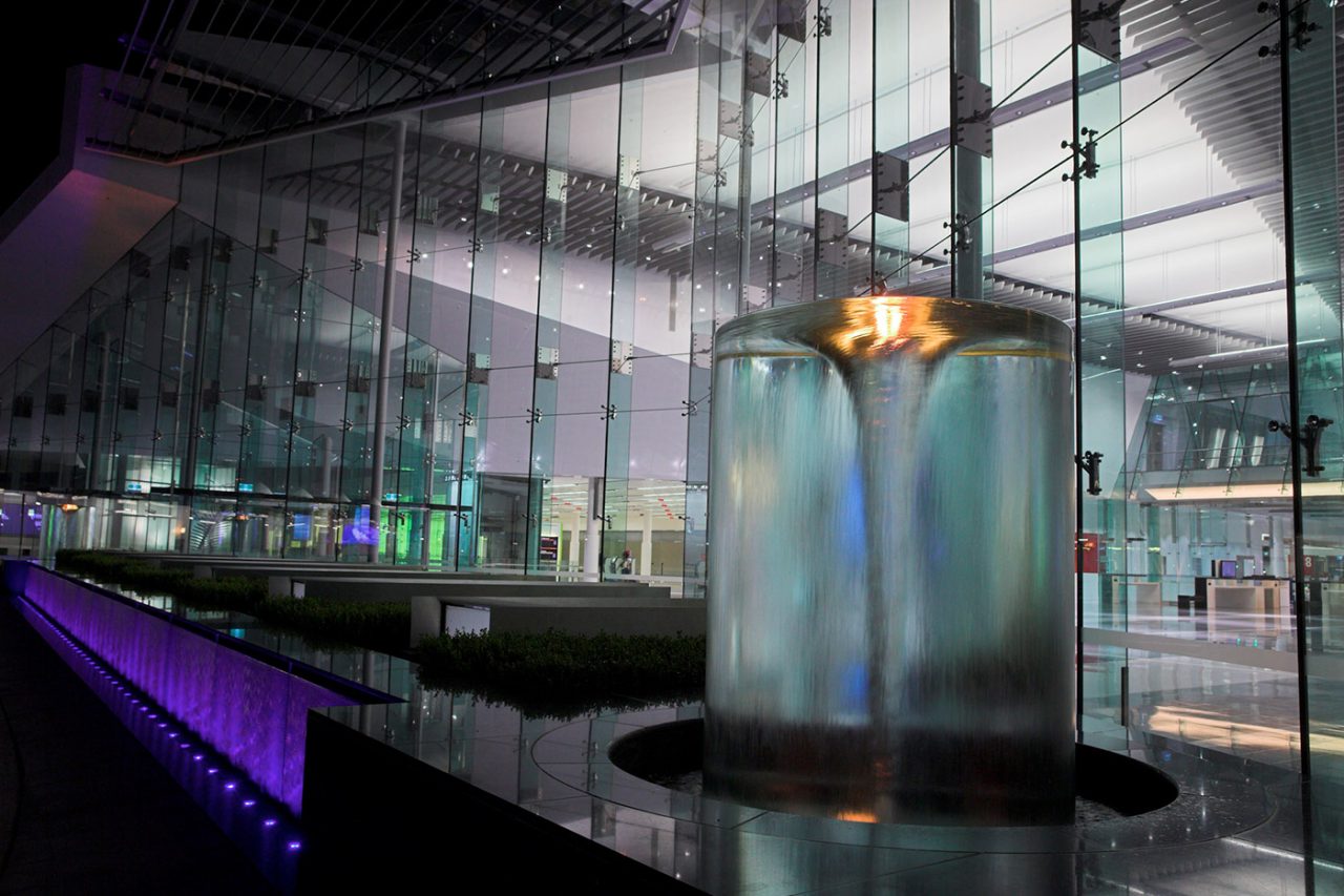 Canberra Airport water feature lit in amber with a purple channel beside the glass facade.