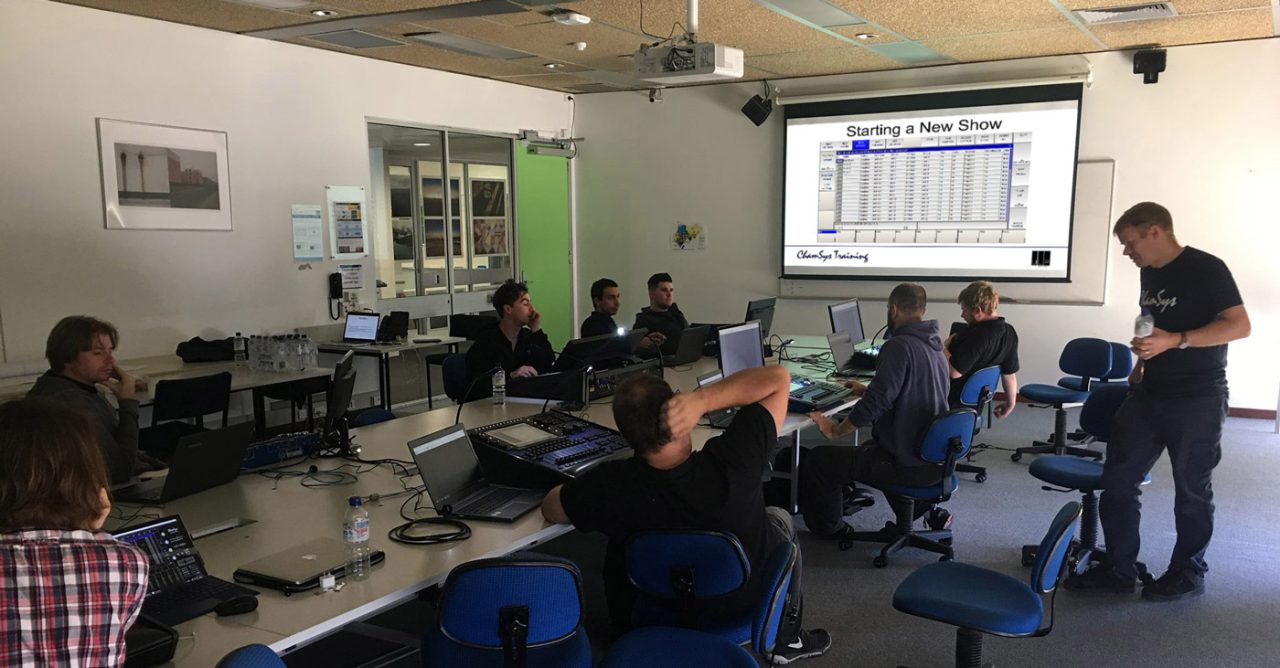 Trainer leading a ChamSys classroom session with laptops and a projected interface.