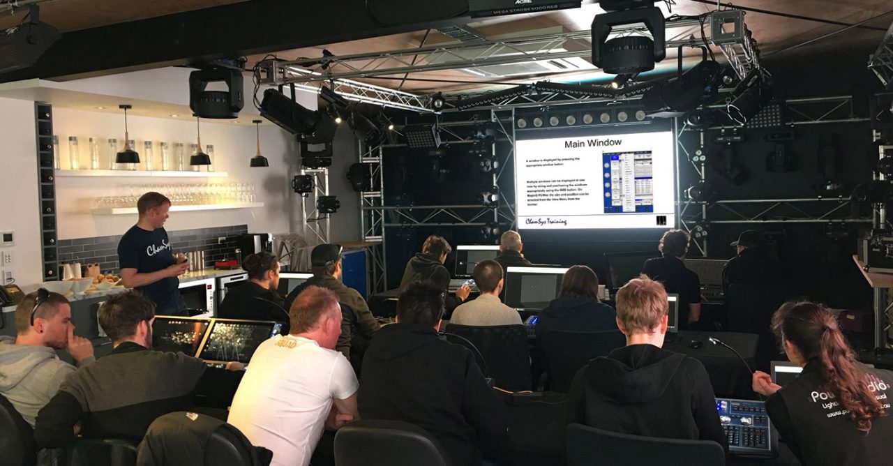 Trainer demonstrating ChamSys software to participants seated at consoles.