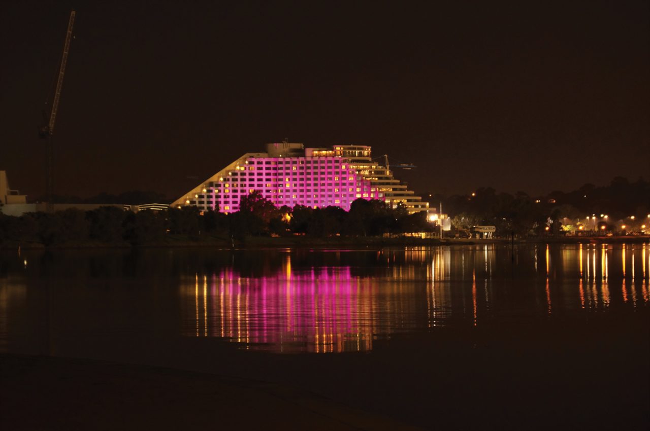 Pink lighting on Crown Perth reflected across the water at night.