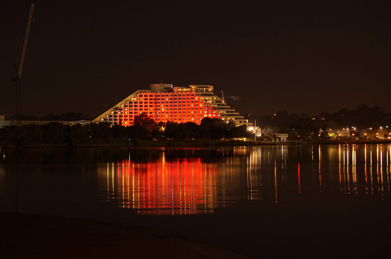 Red and orange lighting on Crown Perth reflected across the water.