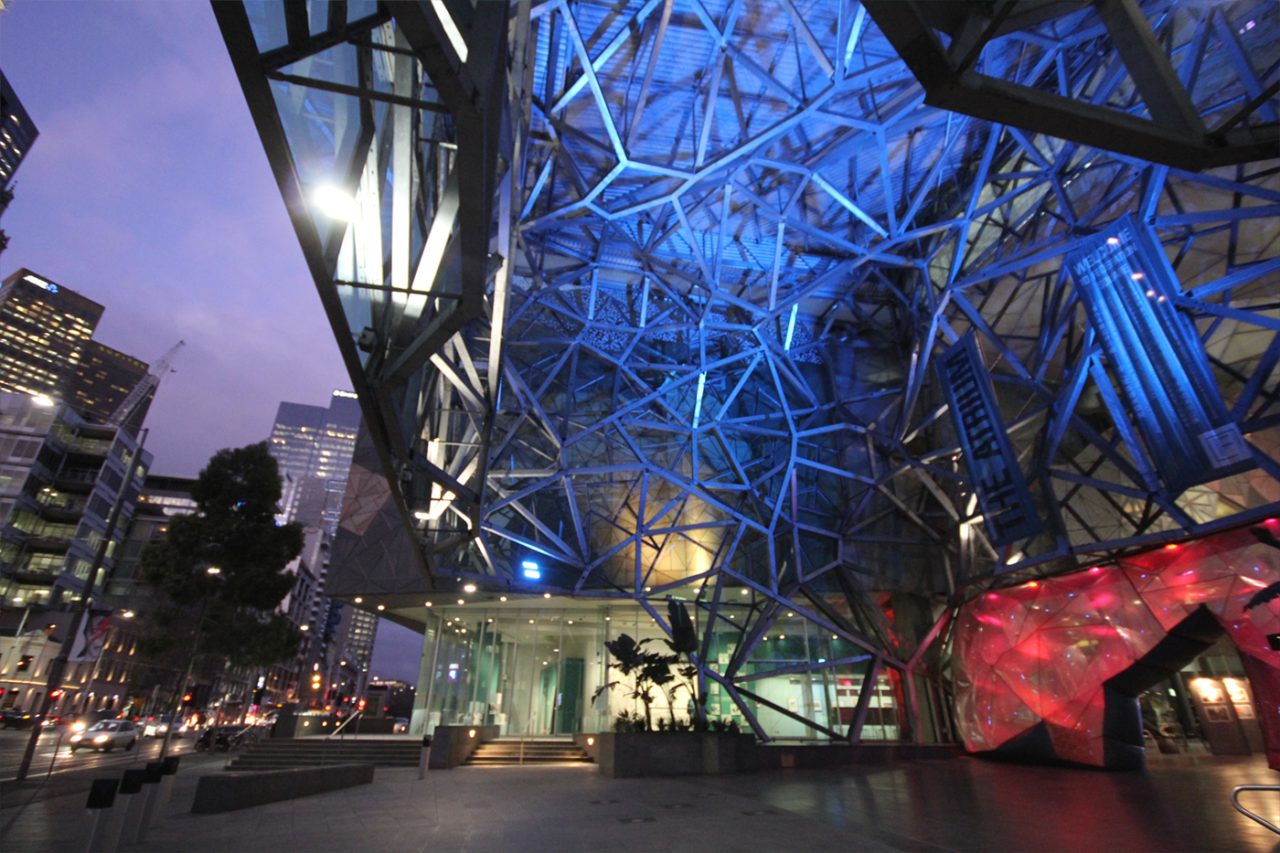Street-side view of Federation Square's blue-lit geometric atrium.