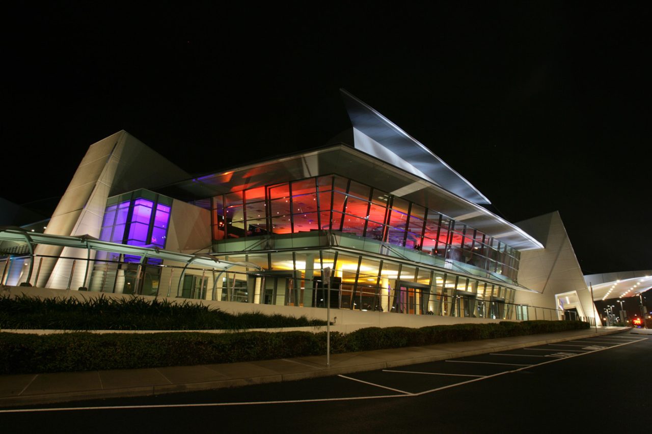 Wide night view of GCCEC with red and purple facade lighting.
