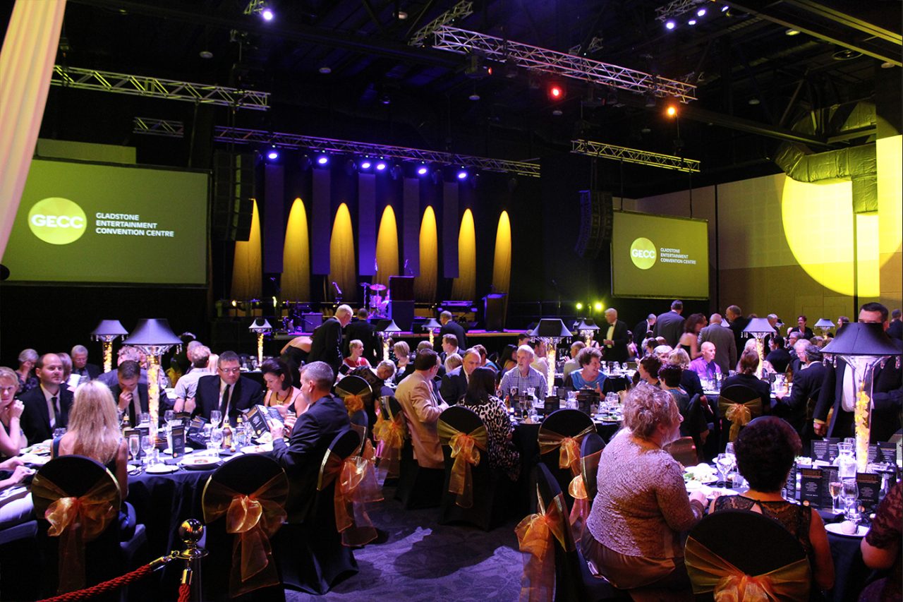 Guests at banquet tables beneath event lighting and screens at Gladstone Entertainment Centre.